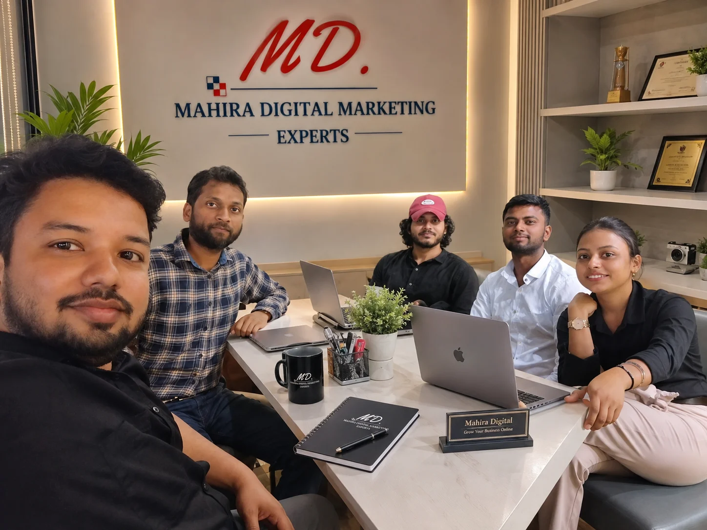 Mahira Digital Marketing Experts team posing together in a modern office with the company logo, laptops, and a professional digital marketing workspace.